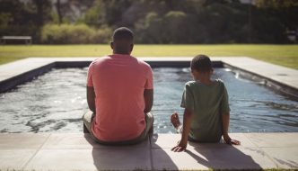 father and son sitting beside pool