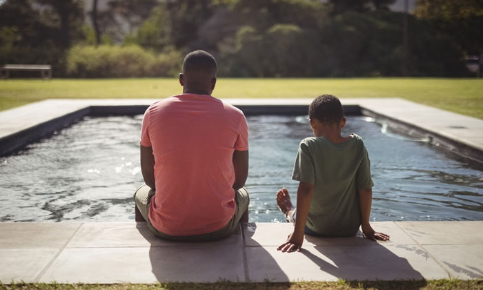 father and son sitting beside pool