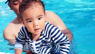 father helping young child experience pool water