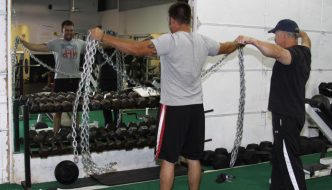 certified fitness instructor helping man lift chains