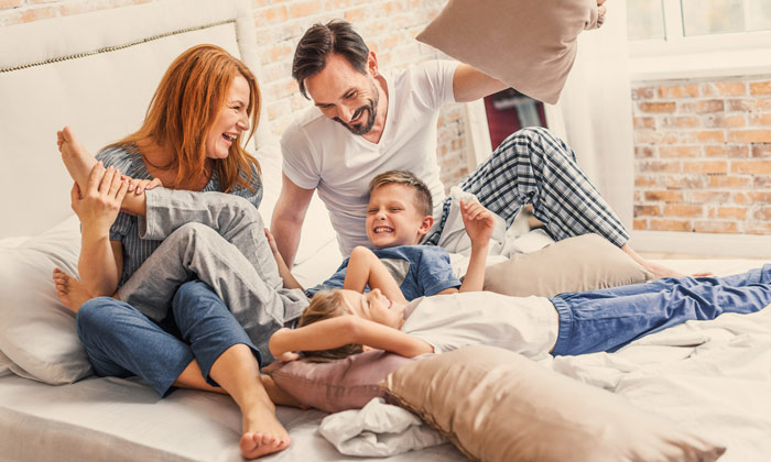 mom and dad having pillow fight on bed with two sons