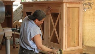 carpenter sanding reclaimed lumber boards on new furniture