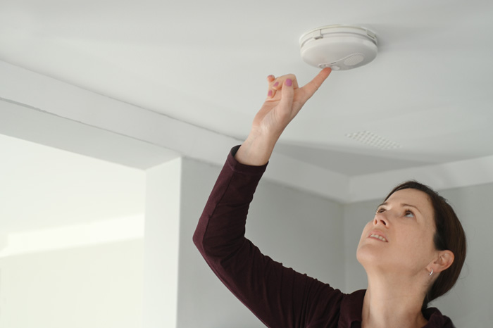 woman pushing button to test smoke detector