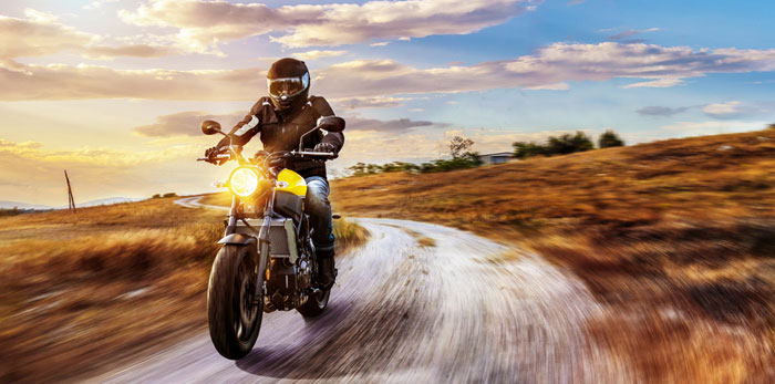 motorcyclist riding fast on country lane through fields