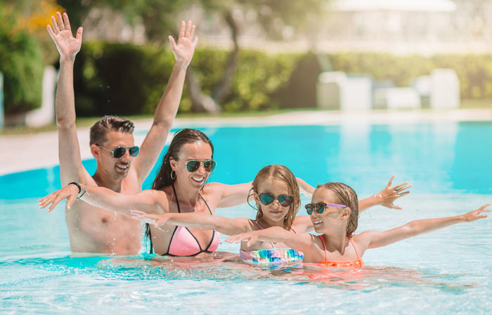 mother and father with two preteen daughters enjoying backyard swimming pool