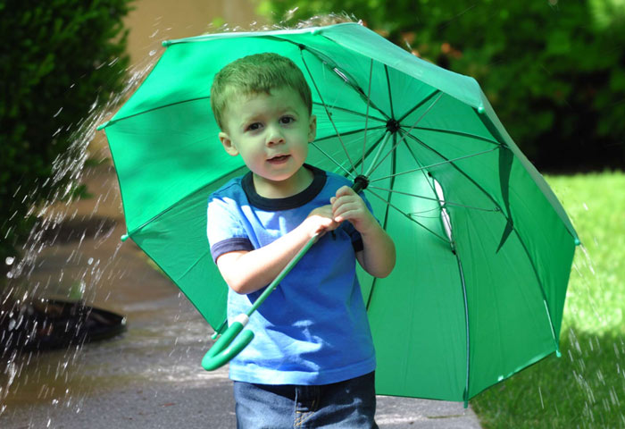 Young boy holding an open umbrella in the rain