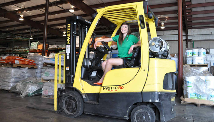 Young woman sitting on a forklift inside a warehouse